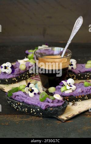 Crostini neri con crema di patate al lilla vitelotte, cipolla a bulbo e pansy cornuto Foto Stock