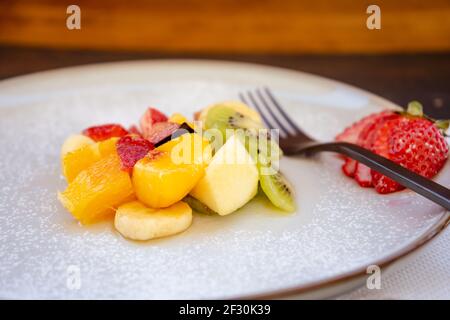 Insalata di frutta naturale e sana con arancia in un piatto gourmet di presentazione su una superficie rustica nera. Concetto di cibo sano, vita sana. 45 gradi Foto Stock