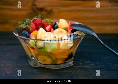 Insalata di frutta naturale e sana con arancia in un recipiente di vetro trasparente, su una superficie rustica nera. Concetto di cibo sano, vita sana. 45 gradi Foto Stock