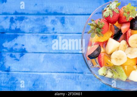 Insalata di frutta naturale e sana con arancia in un recipiente di vetro trasparente, su una superficie rustica - blu. Concetto di cibo sano, vita sana. 45 gradi Foto Stock