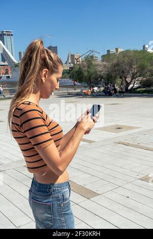 Bella donna latina che controlla e risponde ai messaggi sul telefono cellulare. Foto Stock