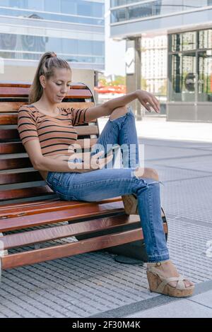 Attraente donna latina che controlla il suo telefono cellulare seduto comodamente una panca Foto Stock