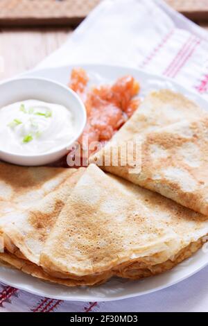 Frittelle sottili con salmone e panna acida su sfondo chiaro. Stile rustico. Foto Stock