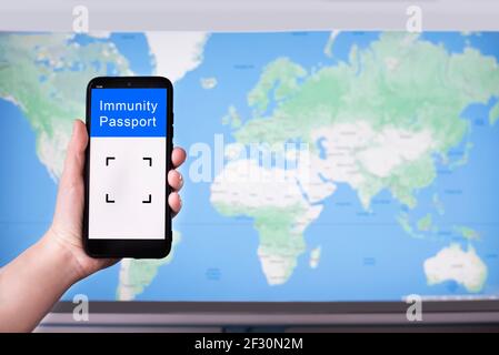 Mano femminile che tiene un telefono cellulare con passaporto di immunità digitale sullo sfondo della mappa del mondo. Covid-19 concetto di viaggio. Foto Stock