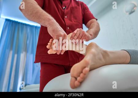 Lavoratore di cura di salute dando orthopedic massaggio ai piedi di donna Foto Stock