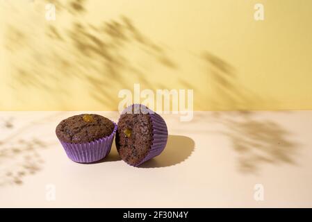 Muffin al cioccolato ai raggi del sole su uno sfondo giallo con belle ombre, primo piano. Foto Stock