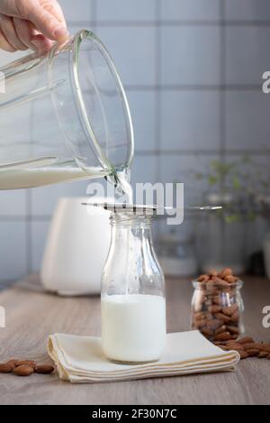 Latte di mandorle fatto in casa utilizzando un frullatore, sforzando il latte attraverso un filtro in un biberon in cucina, primo piano. Foto Stock