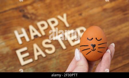 Una mano femminile tiene l'uovo con un viso carino. Buon concetto di Pasqua. Cartolina di vacanza Foto Stock