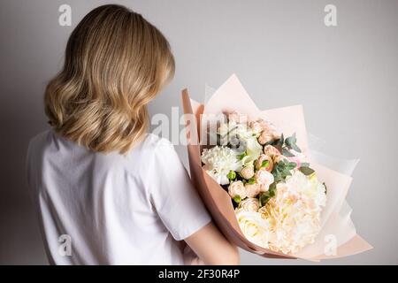 Donna bionda che tiene bouquet di fiori contro parete grigia Foto Stock