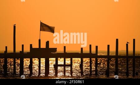 Una bandiera degli Stati Uniti vola su un molo mentre il sole tramonta su Mobile Bay a Fairhope, al, USA, il 14 ottobre 2020. Foto Stock