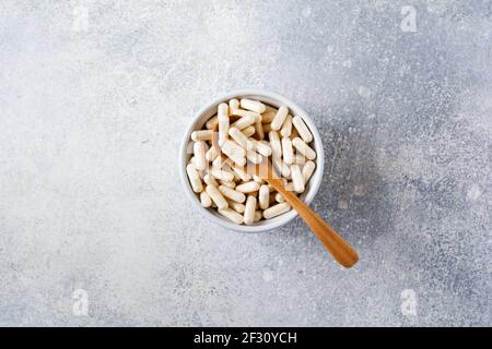 Collagene chiuso in capsule per alimenti dietetici in una ciotola di ceramica su un vecchio fondo grigio di cemento. Disposizione piatta con spazio per la copia Foto Stock