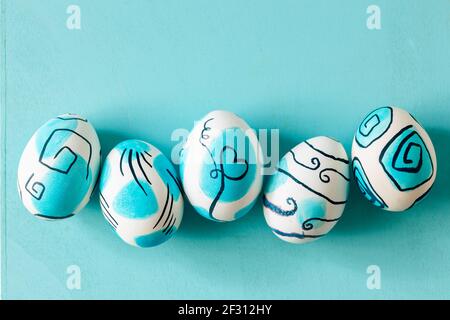 Uova di pasqua dipinte in modo creativo su sfondo turchese. Idee di Pasqua. Foto Stock