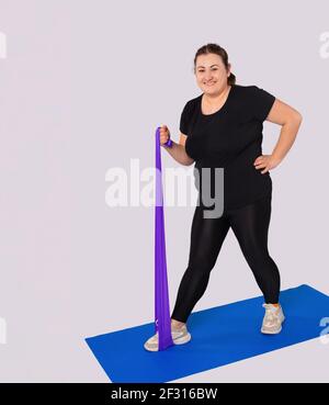 Atletica sorridente grande donna corpo di allenamento a casa, allenamento sportivo attivo. Atleta femminile grasso in abbigliamento sportivo facendo avanti affondi esercizio con elastico Foto Stock