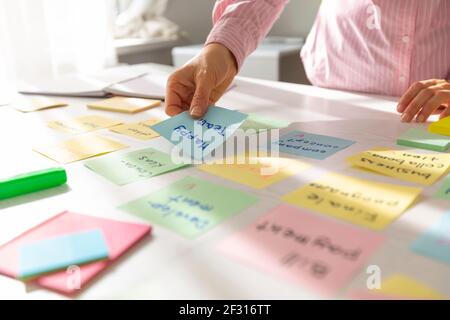 Donna d'affari che lavora su un progetto utilizzando note appiccicose sul suo desktop. Brainstorming per trovare nuove idee per lo sviluppo dell'azienda. Foto Stock