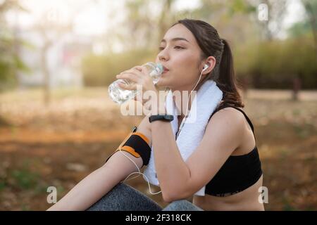 La giovane atleta prende una pausa, acqua potabile, fuori su una corsa in una giornata calda. Foto Stock