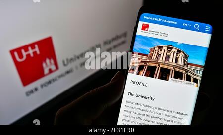 Persona che tiene il cellulare con la pagina web dell'università tedesca Universität Amburgo (UHH) sullo schermo davanti al logo. Mettere a fuoco il centro del display del telefono. Foto Stock