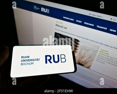 Persona che detiene smartphone con il logo dell'università tedesca Ruhr-Universität Bochum (RUB) sullo schermo di fronte al sito web. Mettere a fuoco il display del telefono. Foto Stock