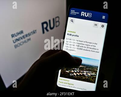 Persona che detiene cellulare con pagina web dell'università tedesca Ruhr-Universität Bochum (RUB) sullo schermo davanti al logo. Mettere a fuoco il centro del display del telefono. Foto Stock