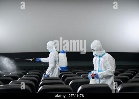 Due lavoratori in abiti speciali pulizia sala cinema con disinfettanti. Concetto di preparazione sala cinema per i visitatori. Foto Stock