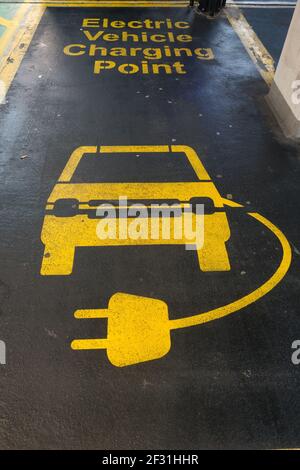 Sono visibili i contrassegni di linea in un vano di parcheggio in giallo su un asfalto nero di un'auto e il cavo di ricarica elettrico. Foto Stock