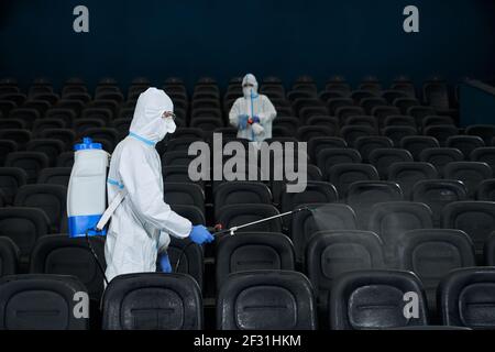 Lavoratori in indumenti protettivi anti-virus pulizia sala cinema con speciali disinfettanti. Concetto di sala di disinfezione. Foto Stock