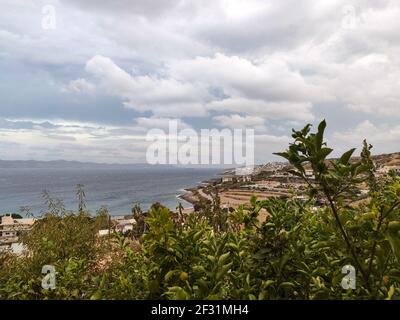 Il cielo epico e grigio tempesta sul villaggio del mare greco con alberi di limone verdi. Estate spettacolare vista panoramica sulla riva del mare Egeo in Grecia Foto Stock