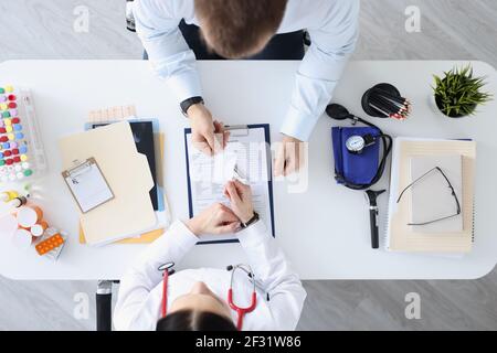 Il medico passa il biglietto da visita al paziente al tavolo di lavoro Foto Stock