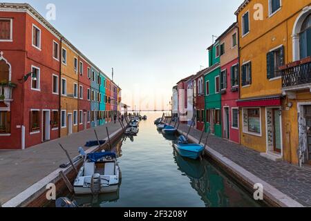 L'isola veneziana di Burano, barche ormeggiate su un canale, case colorate e negozi al crepuscolo con la gente sui marciapiedi. Foto Stock