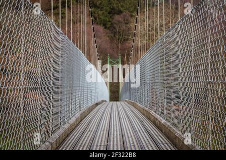 Vista su un ponte sospeso in legno che conduce a una foresta woodland in scozia Foto Stock