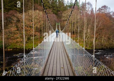 Uomo che cammina su un vecchio ponte sospeso in legno attraverso il fiume Deugh a Dundeugh, vicino a Kendoon, Dumfries e Galloway, Scozia Foto Stock