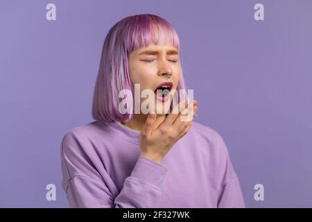 Donna stanca sonnolenta sbadiglia, ricopre la bocca con la mano. Molto noioso, poco interessante. Sfondo viola studio. Foto Stock