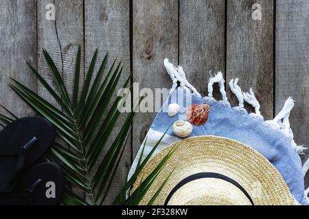 Concetto di viaggio o vacanza, fine settimana. Cappello di paglia con foglia di palma, scarpe e asciugamano, conchiglie di mare su sfondo di legno. Tempo di relax. Pho di alta qualità Foto Stock