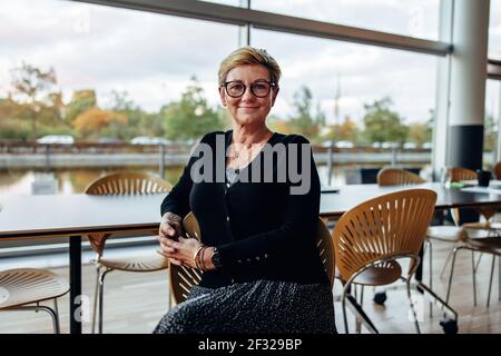 Ritratto di una donna d'affari di successo seduta sulla sedia in una caffetteria d'ufficio. Professionisti aziendali senior che guardano con sicurezza alla fotocamera. Foto Stock