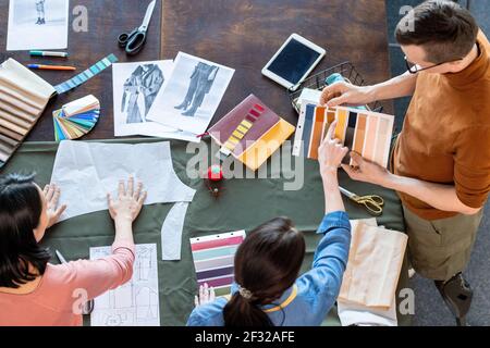 Gruppo di giovani stilisti che discutono di campioni tessili per il nuovo collezione stagionale, mentre la donna bruna indica uno di loro Foto Stock