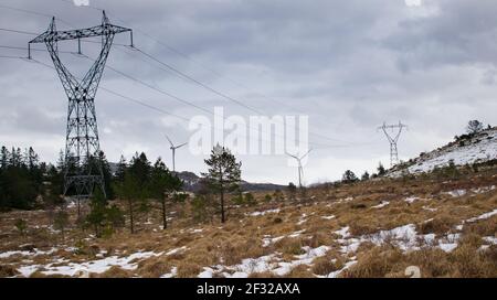 Mulino vicino alle linee elettriche durante l'inverno in Norvegia. Concetto di energia pulita Foto Stock