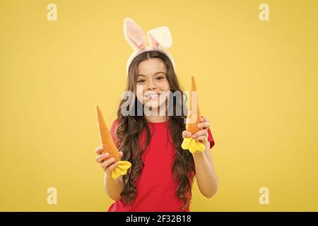 Tradizione primaverile. Orecchie conigliate per bambini. Dieta per la salute. Beneficio di mangiare la carota. Carota di Pasqua. Ragazza tenere carota. Gioca con il cibo. Giallo bambino Foto Stock