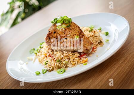 Cibo cotto su un piatto bianco - tonno servito su risotto vegetale. Foto Stock