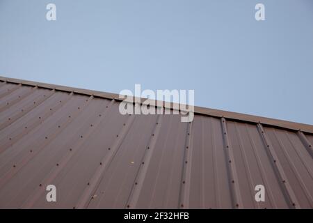 un nuovo tetto in metallo con bulloni taglia diagonalmente su incorniciate uno skyline blu chiaro Foto Stock