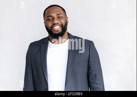 Ritratto di bell'uomo d'affari in elegante abito formale su sfondo bianco. Il giovane adulto africano americano è in piedi in ufficio, guardando direttamente la macchina fotografica, sorridendo Foto Stock