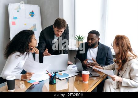 Colleghi multirazziali concentrati a lavorare insieme sul progetto, discutendo le domande sul lavoro. Eleganti uomini d'affari alla conferenza, seduti in ufficio, imparando grafici finanziari Foto Stock