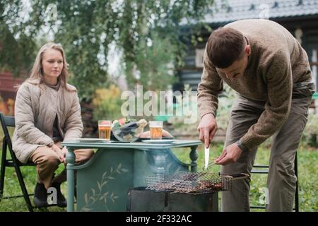 Un giovane dell'europa orientale prepara un barbecue, arrostisce la carne fragrante sulla griglia. Concetto di un picnic romantico per una giovane coppia. Foto Stock