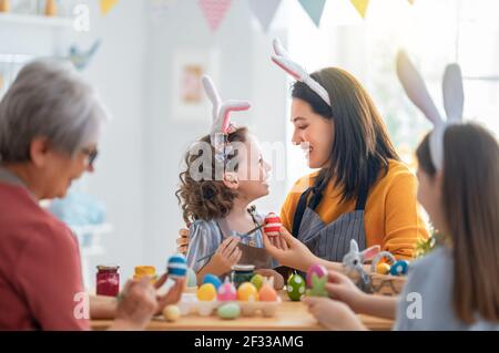 Madre, nonna e bambini stanno dipingendo le uova. Buona famiglia si prepara per Pasqua. Carino bambine che indossano orecchie conigliate. Foto Stock