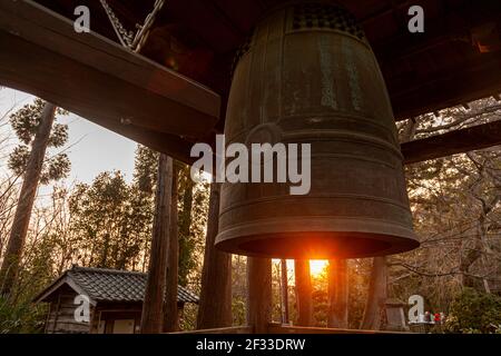 Grande campana di ottone in un tempio giapponese Shinto a Sendai, Giappone chiamato Rinno-ji Tempio con alberi e il tramonto sullo sfondo Foto Stock