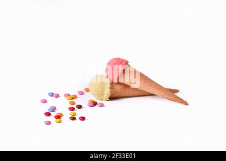 Un assortimento di bottoni di cioccolato multicolore con coni di gelato alla vaniglia e alla fragola. Messa a fuoco selettiva. Concetto di cioccolato e gelato. Foto Stock