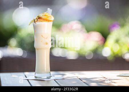 Cocktail PinaColada o Milkshake con padelle e arancio sulla parte superiore servito in un bicchiere alto su una terrazza estiva. Foto Stock