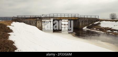 Fiume in primavera sulla riva della neve. Vecchio ponte sul fiume. La neve si scioglie con l'arrivo di calore vicino alle rive del fiume. Nel Foto Stock