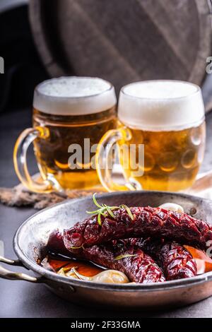 Salsicce calde alla griglia servite in una padella calda accanto a due birre alla spina. Foto Stock