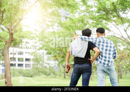 Vista posteriore di due giovani amici in piedi con la birra e. parlare all'aperto Foto Stock