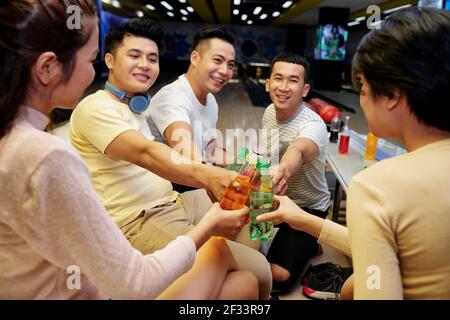 Gruppo di amici che brinda con bevande e si diverte insieme durante la partita di bowling Foto Stock