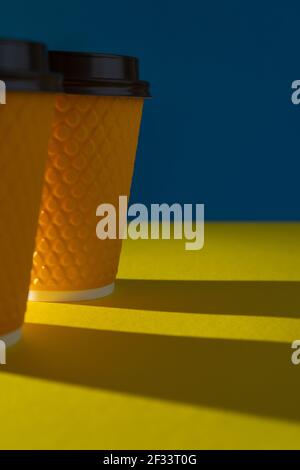 Tazza di carta gialla a coste con coperchio in plastica per bevande da asporto nei fast food. Una tazza di caffè, cioccolata, tè da un caffè in strada. Inserire il testo. Sfondo blu. Foto Stock